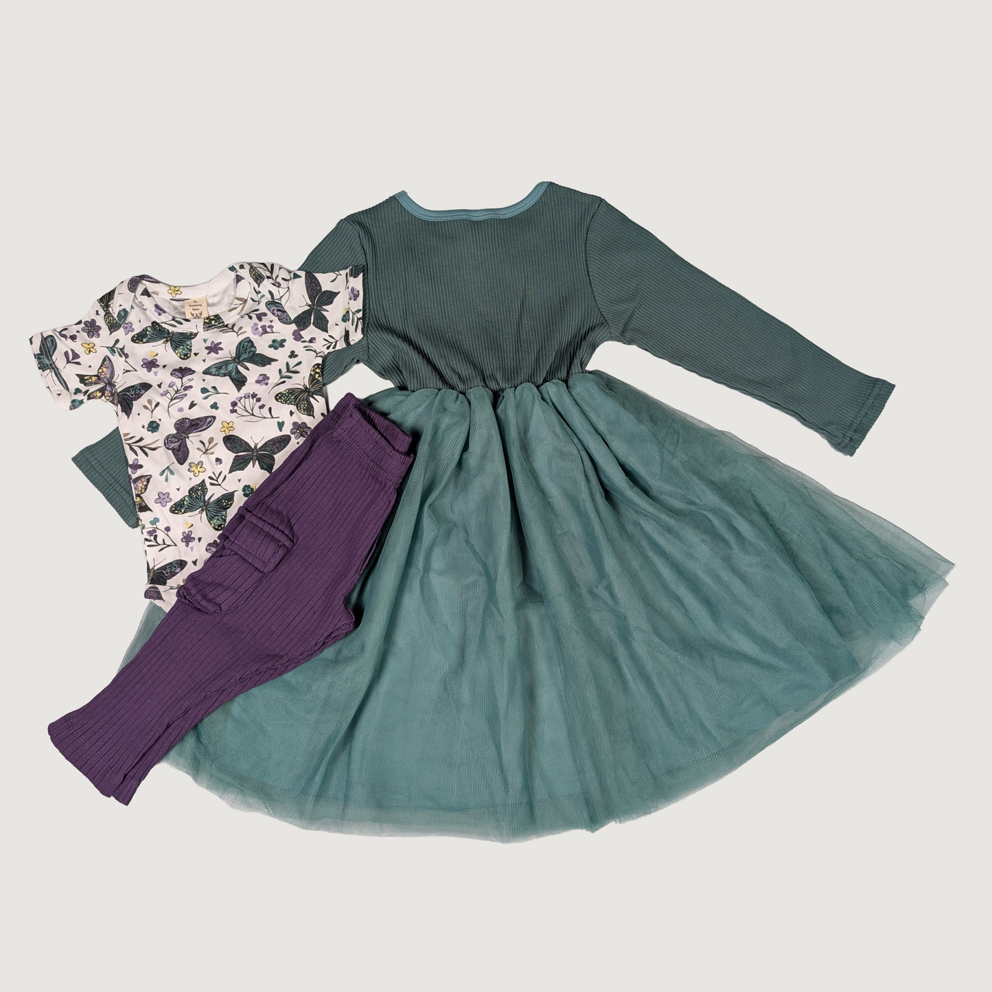 Teal dress with long sleeves, purple leggings, and a butterfly-patterned shirt on a light gray background